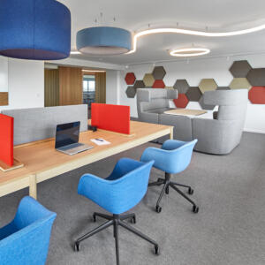 Moderne Büroeinrichtung mit roten Akustikelementen, ergonomischen Stühlen und Workbench als Arbeitstisch, die eine kreative und funktionale Arbeitsumgebung darstellt.